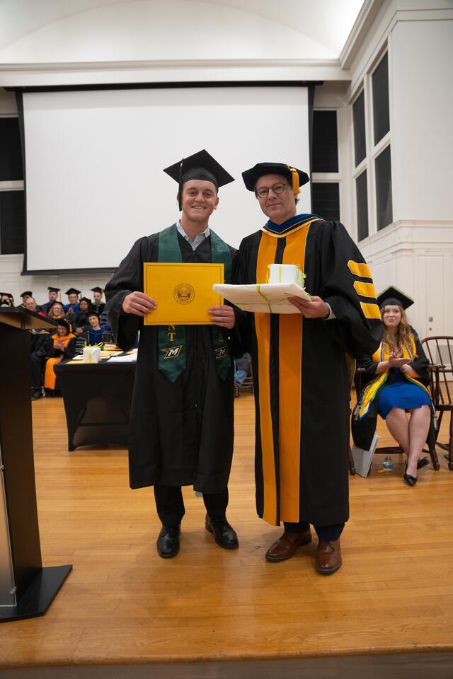Student in graduation regalia poses with Provost Flavius Lilly, also in graduation regalia