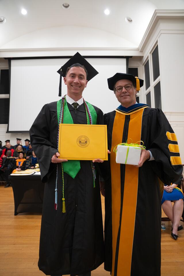 Student in graduation regalia poses with Provost Flavius Lilly, also in graduation regalia