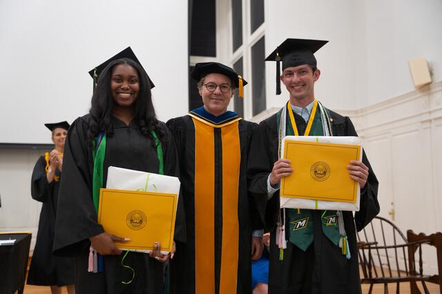 Student in graduation regalia poses with Provost Flavius Lilly, also in graduation regalia
