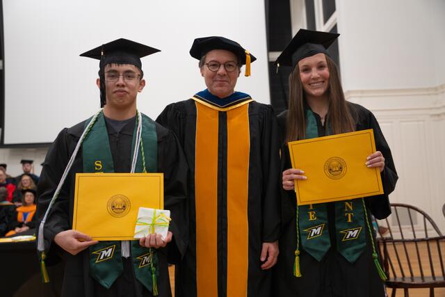 Students in graduation regalia poses with Provost Flavius Lilly, also in graduation regalia
