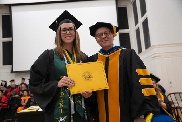 Student in graduation regalia poses with Provost Flavius Lilly, also in graduation regalia