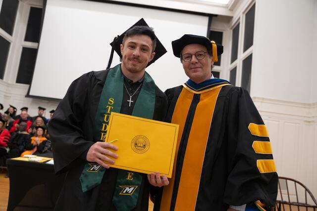 Student in graduation regalia poses with Provost Flavius Lilly, also in graduation regalia