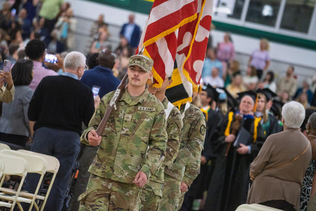 A U.S. Army ROTC color guard member carries a rifle while leading the flag procession into McDaniel College commencement.