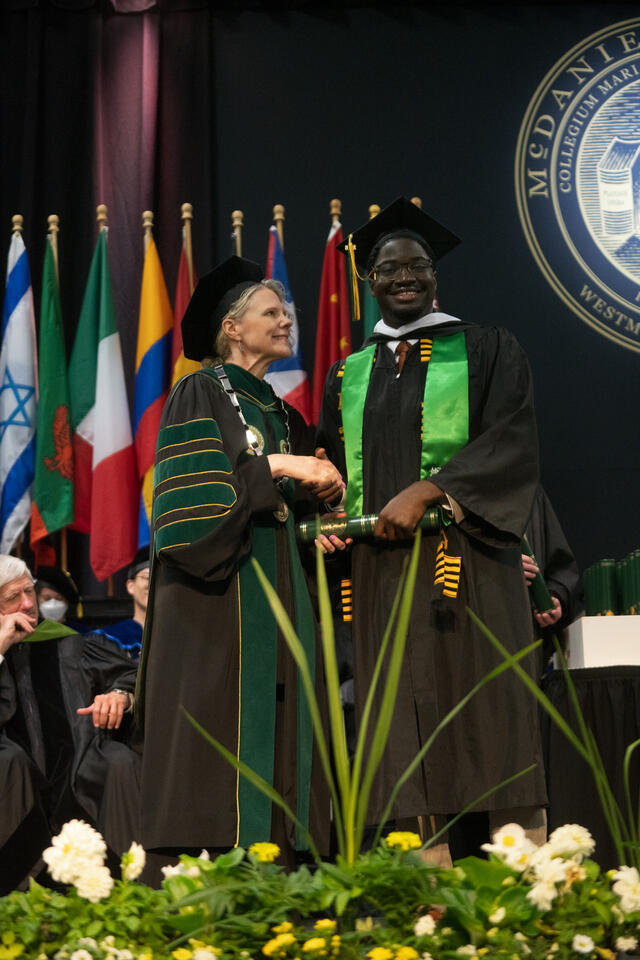 McDaniel's president hands a diploma scroll to a graduate 