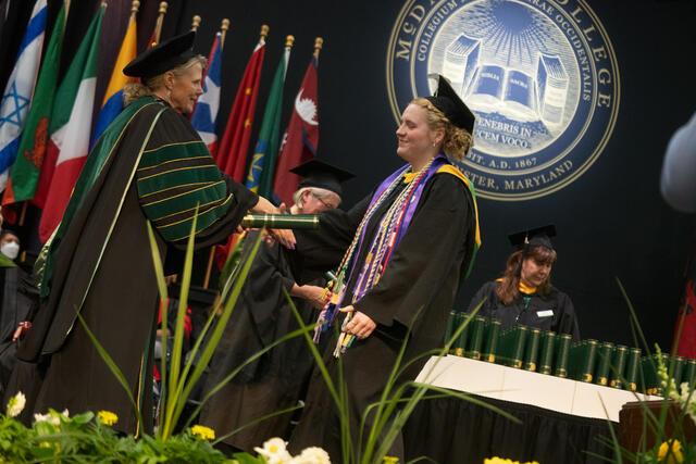 McDaniel's president hands a diploma scroll to a graduate