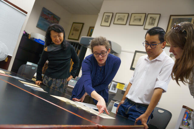 A group of people gather around a table with historical artifacts on it.