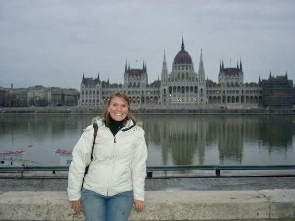 A young woman dressed for cold weather stands in front of a landmark in Budapest.