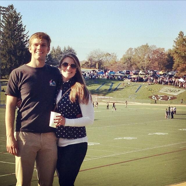 A young man and a young woman smile in front of McDaniel's football stadium.