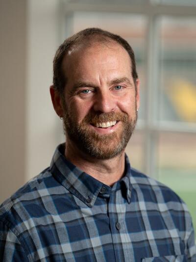 Photo of a man in a plaid shirt standing in front of a window.