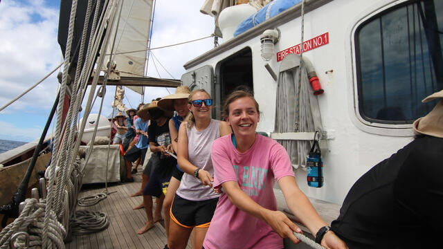 Riley Palmer '18, in a pink shirt, helps raise the main sail on board the SEA Semester ocean research vessel, Robert C. Seamans.