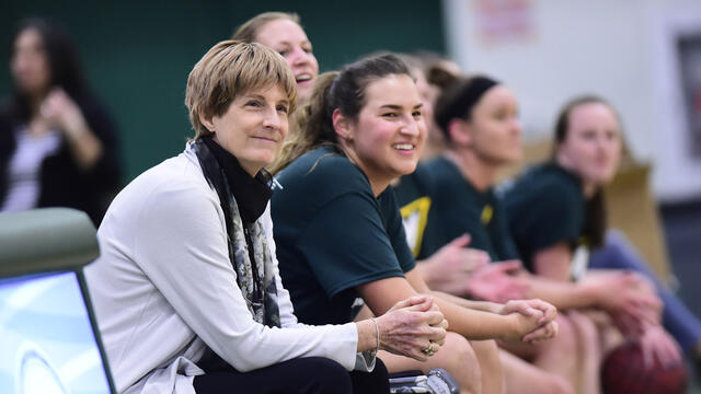 Coach Becky Martin sitting with basketball players on the sidelines.
