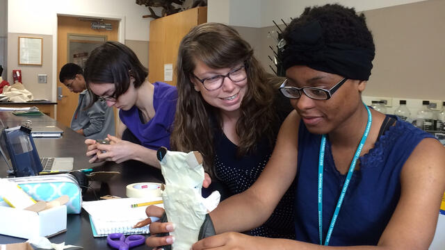 Favour Ubani (right) discusses her cell phone holder with professor Katie Staab while classmate Jillian Stewart works in the background.