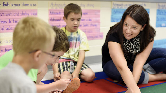 Student interacting with elementary school children on carpet.