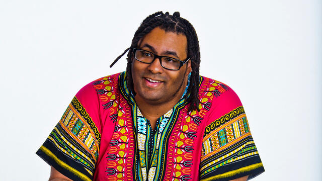 Wayne Young leaning on table flipping through pages of a book in front of a white background.
