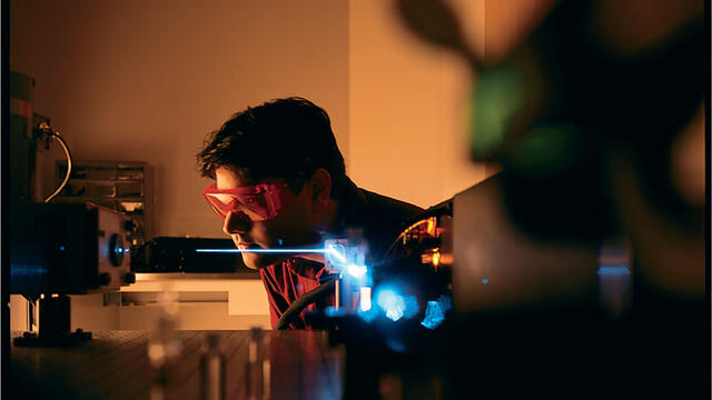 Student wearing goggles in a dark lab using lasers.