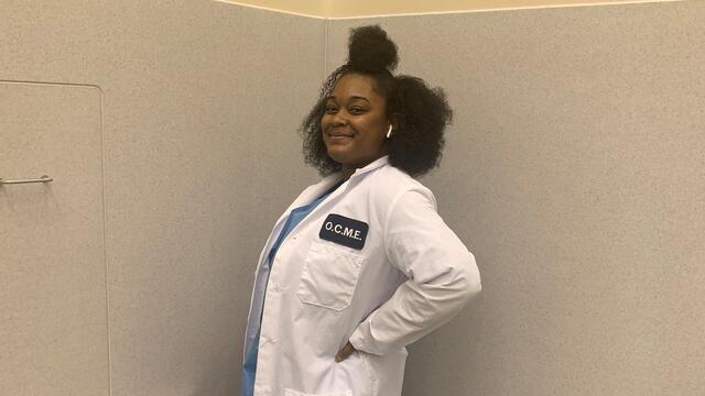 Alumni Treyana Johnson standing in her OCME lab coat.