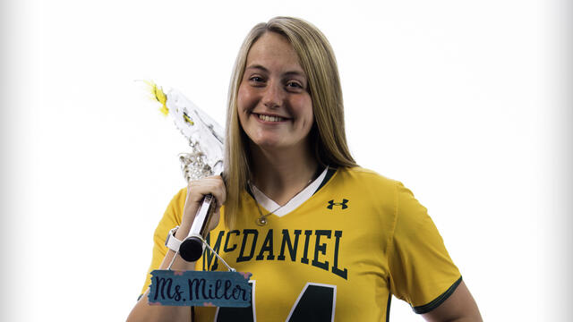 Hannah Miller poses with a lacrosse stick and a "Ms. Miller" name tag.
