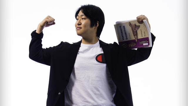Hyosik Kim flexes his arms above his head while holding a science textbook.