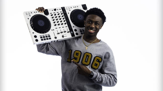 Kekuta Bah poses with a DJ board on his shoulder.
