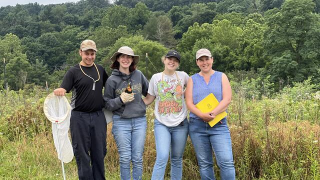 Three students pose with Holly Martinson in a field.