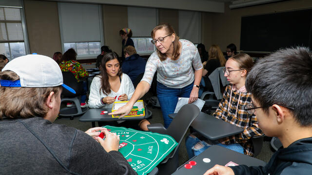 A group of students plays Tripoley in a classroom. The professor points at the board.
