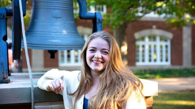 A blonde woman standing by a bell outside 