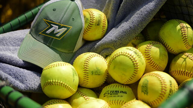 Photo of a green McDaniel hat with an M on the front on top of a towel and bright yellow softballs.