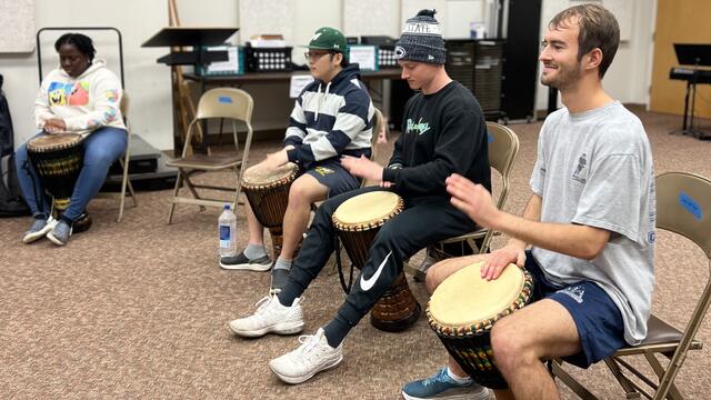 Photo of students playing drums in a classroom.