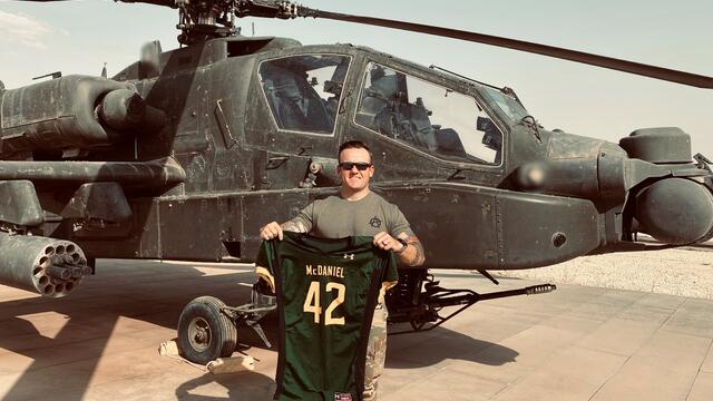 Nick Giusti holds up a McDaniel football jersey in front of a helicopter while stationed in Syria.