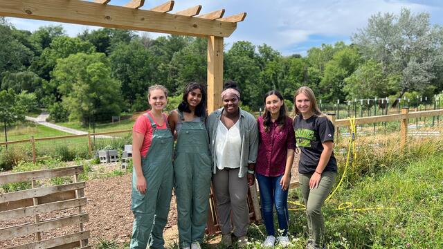 Four students pose with professor Elly Engle in front of a vegetable garden at the McDaniel Environmental Center.