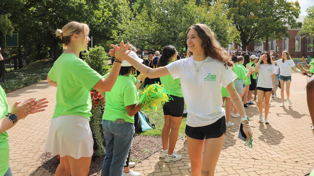 A first-year, female student in a white t-shirt high fives with a female peer mentor in a green t-shirt.