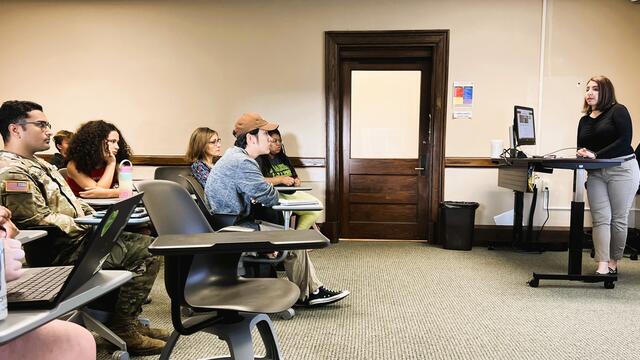 A woman speaks to students seated in a classroom.