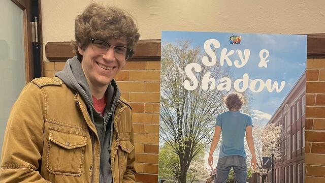 A man stands next to a poster reading "Sky and Shadow."