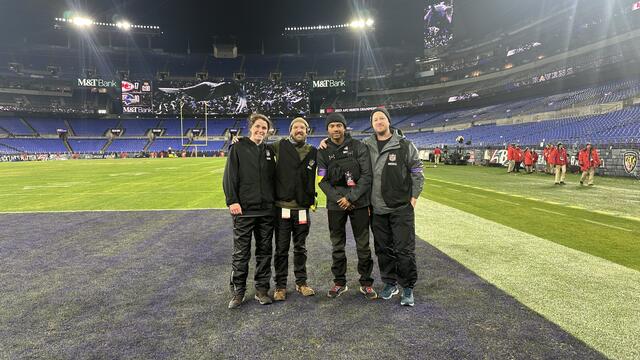 Four people stand on the Baltimore Ravens stadium end zone.
