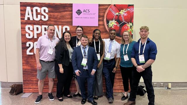 McDaniel students and faculty pose for a group photo in front of an ACS conference sign