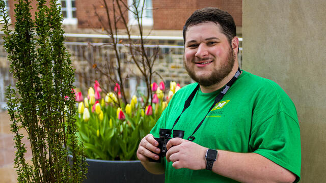 A student stands outside holding binoculars.