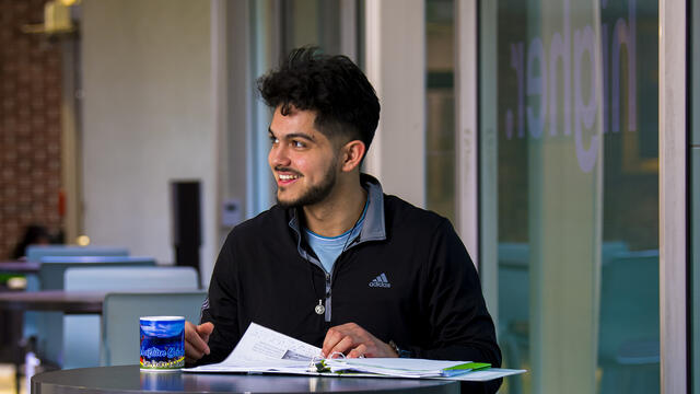A student sits at a table with a notebook in front of him.