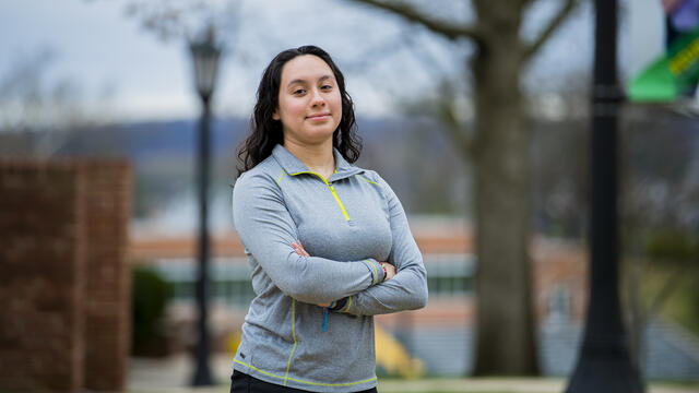 A student stands with her arms crossed outside.