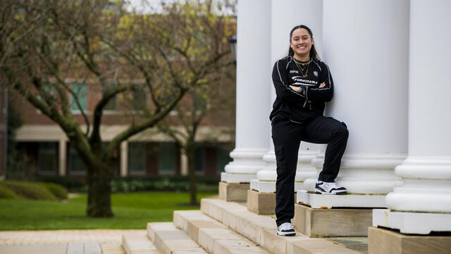 A student leans against a white column outside.