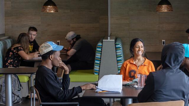 A group of students laughs at a table in the dining area of Roj Student Center.