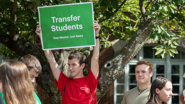student wearing red shirt holding up sign that says "Transfer Students"
