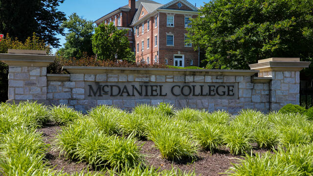 brick entry way sign that says McDaniel College with campus buildings in the background