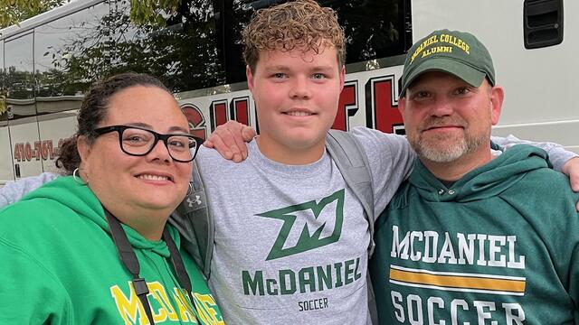 Marcie Mason, Luke Mason, and Pete Mason stand together outside while wearing McDaniel soccer shirts.