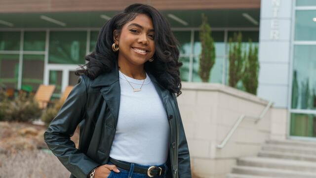 Portrait of Janiah Fields outside of the student center wearing a white T-shirt, jeans, and a black leather blazer.