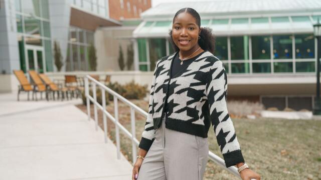 Olivia "Kaami" Effa stands outside of the student center wearing a black and white patterned cardigan and tan slacks.