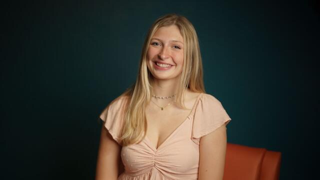 Headshot of Madge Myers on an orange couch while wearing a pink blouse.