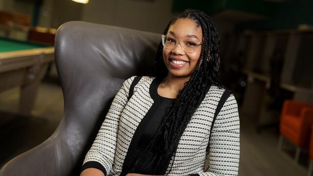 Nakayla Lawson sits in an armchair, wearing a black shirt and a black and white striped blazer.