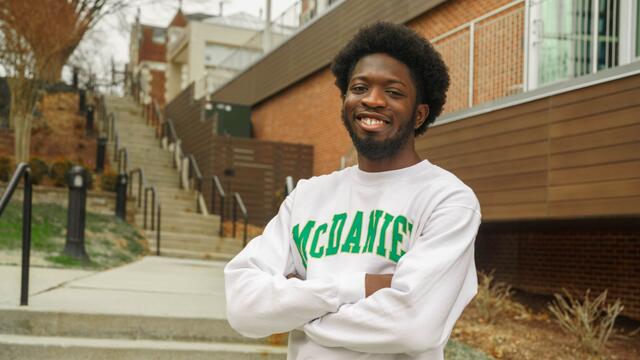 Olanrewaju Oluwaseyi Abayomi stands outside in front of a staircase with his arms crossed, wearing a McDaniel College sweatshirt.