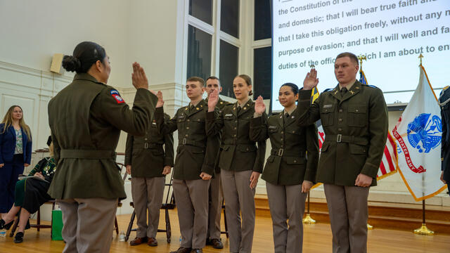 Four cadets in a row hold up a hand while reciting their oath at Commissioning.