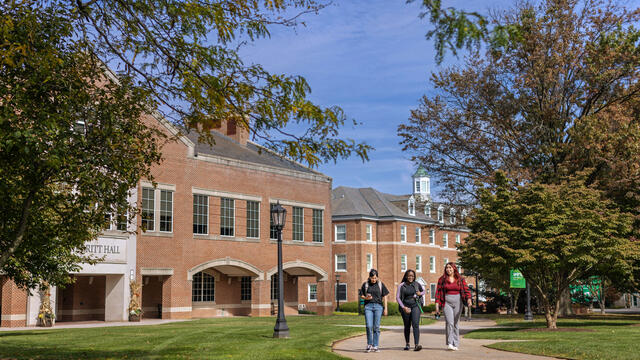 Three students walking down a pathway in front of Merritt Hall in the springtime.